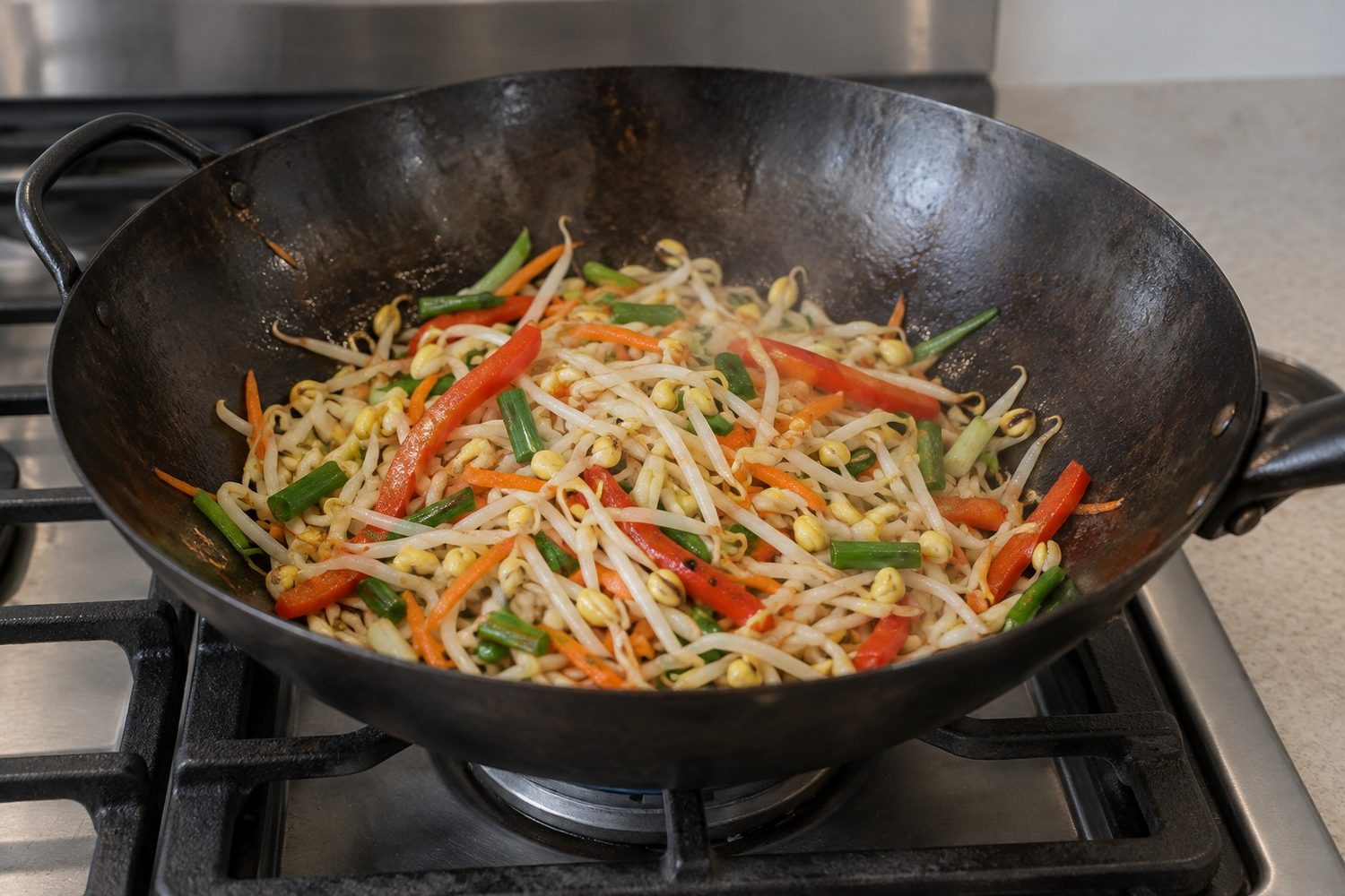 Wok on a stovetop holding pale thick mung bean sprouts cooking with sliced carrots, peppers and green onion, with light steam rising