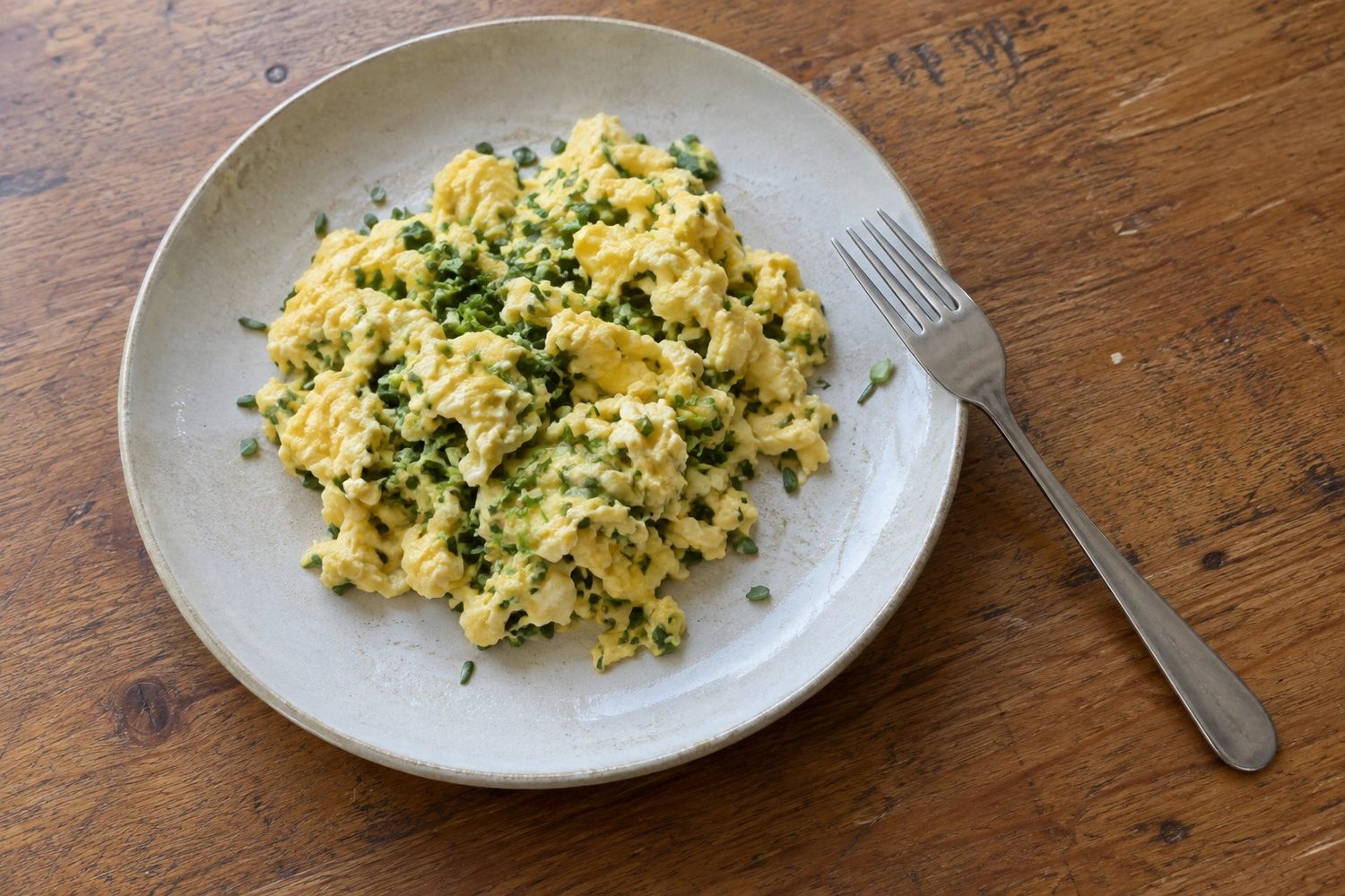 Plate of soft scrambled eggs with finely chopped green microgreens mixed through and a fork resting on the plate edge on a kitchen table